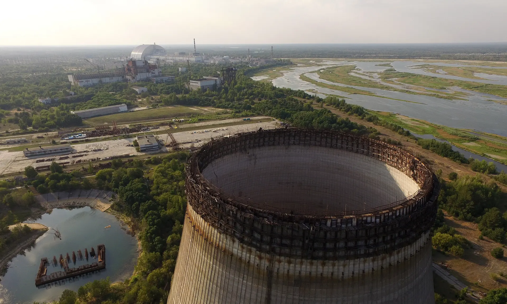 Частично построенная и заброшенная градирня в Чернобыле в качестве защитного ограждения в дали возвышается над повреждённым реактором номер четыре